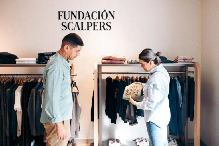 Dos personas revisando una prenda en una tienda de ropa con estanterías y percheros organizados.